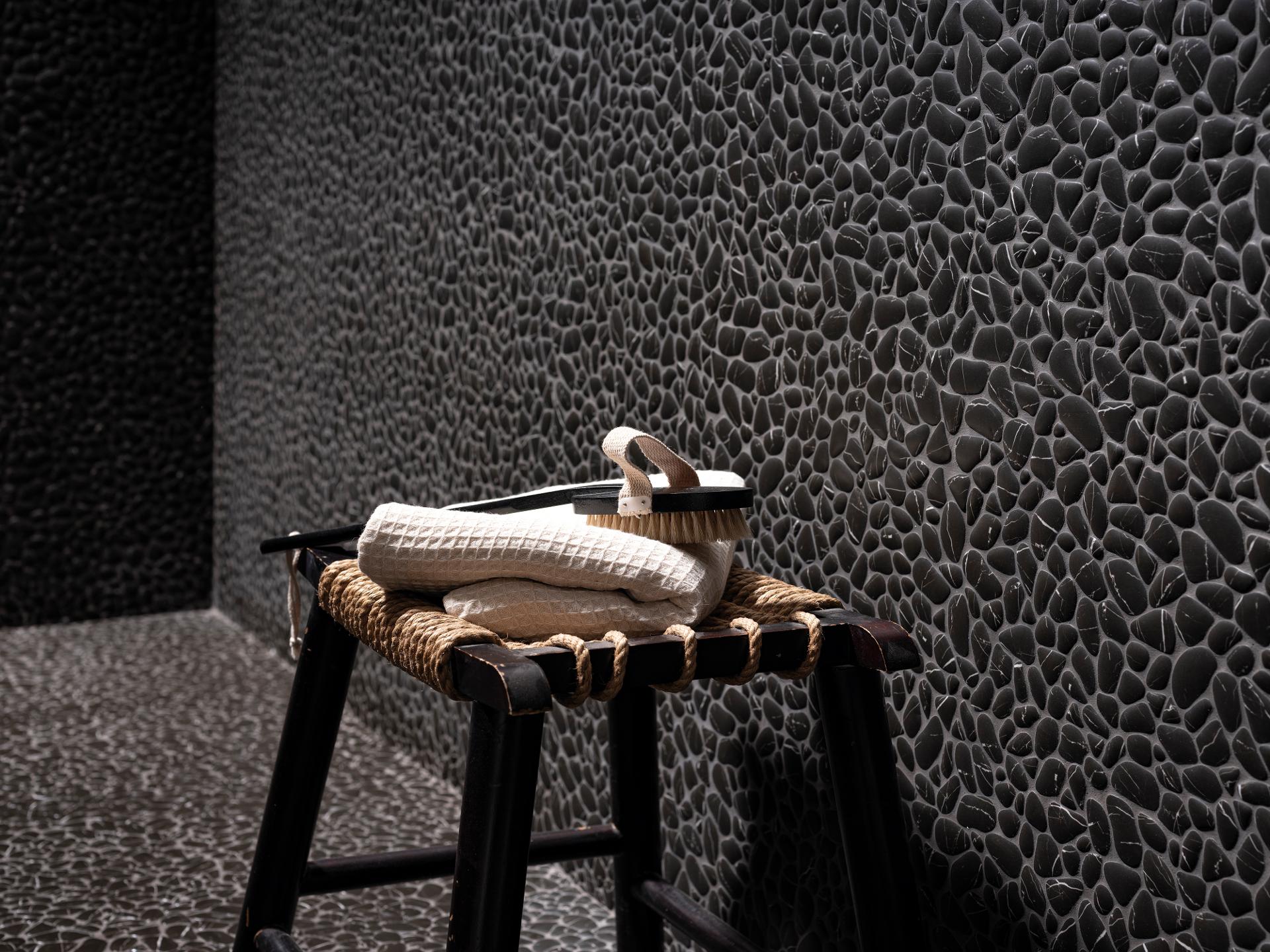 Vägg av svart pebble-mosaik med en pall, vikta handdukar och en borste
